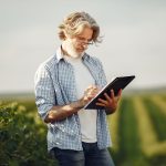 Produtor rural anota informações enquanto observa uma plantação.
