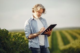 Produtor rural anota informações enquanto observa uma plantação.