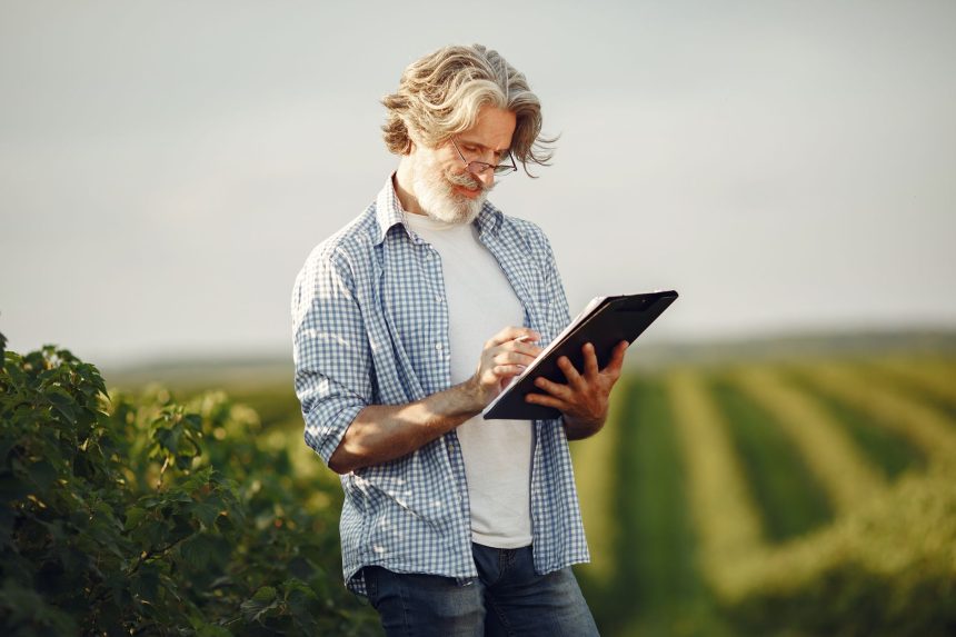 Produtor rural anota informações enquanto observa uma plantação.