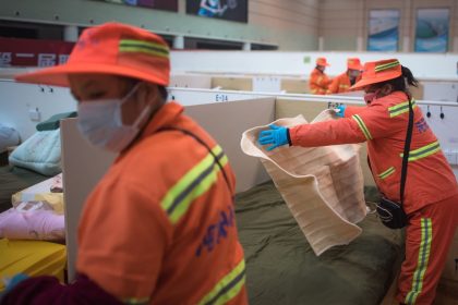 Profissionais equipados organizam leitos temporários em uma unidade interna de atendimento emergencial.