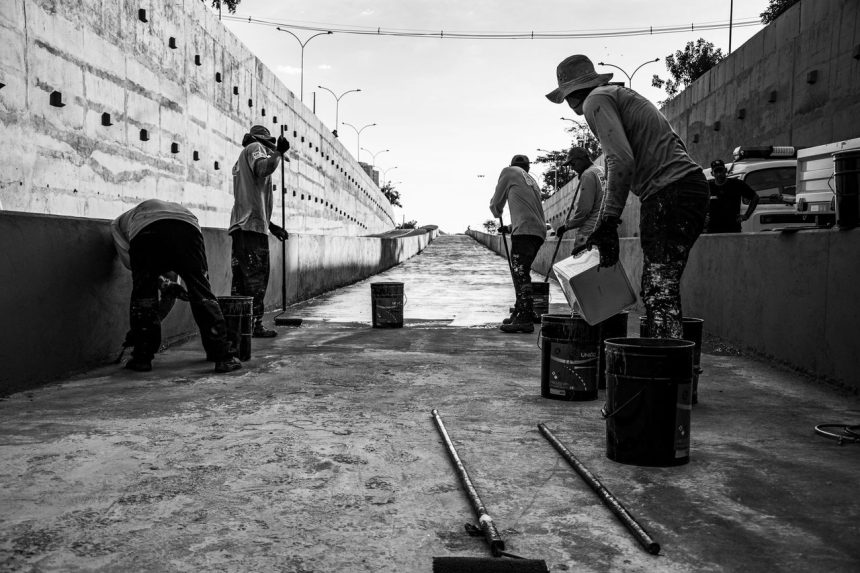 Grupo de trabalhadores limpa uma passagem de concreto em espaço público.