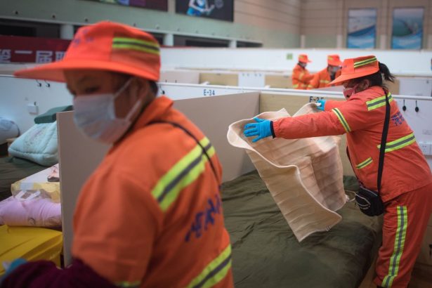Profissionais equipados organizam leitos temporários em uma unidade interna de atendimento emergencial.